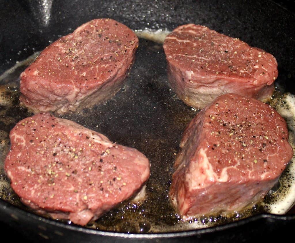 4 beef tenderloin steaks cooking in cast iron skillet