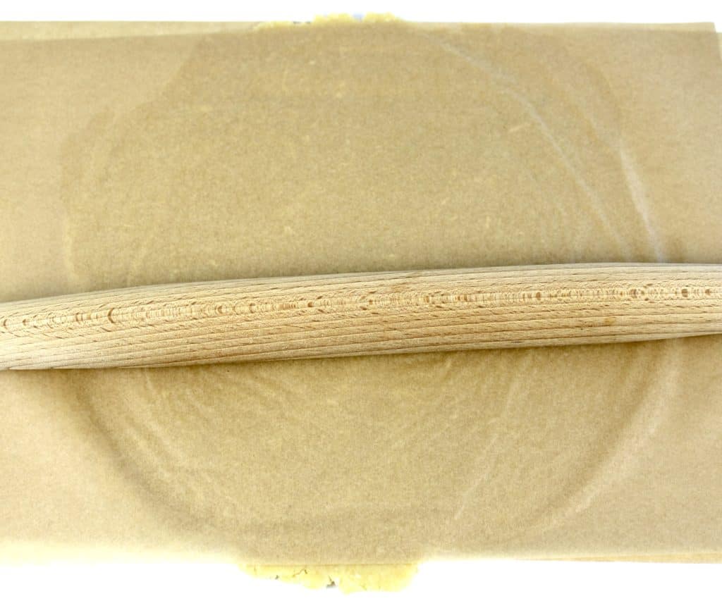 pie crust dough in parchment paper with rolling pin on top