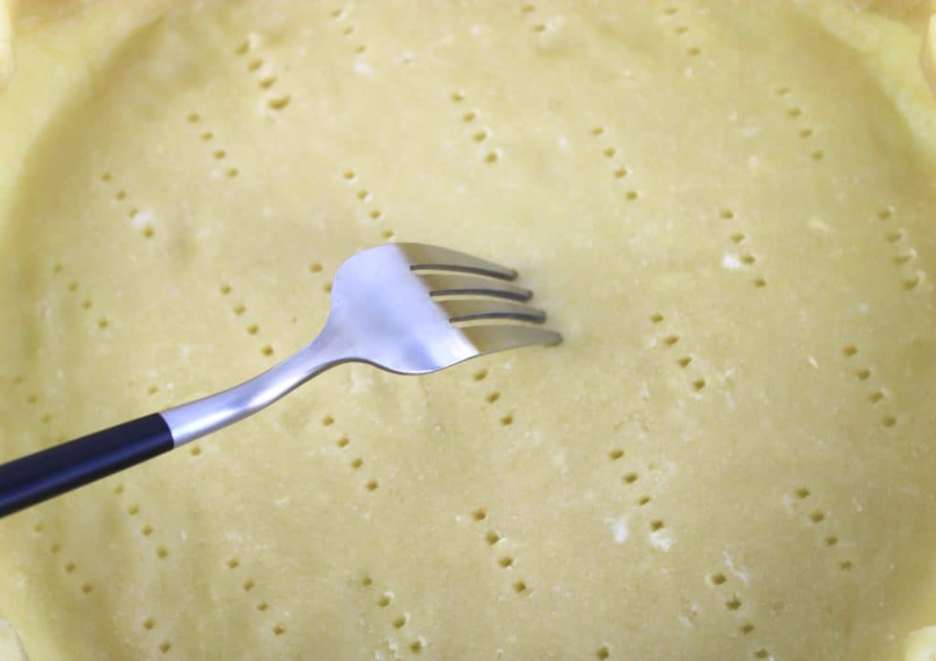 closeup of pie crust with fork pricking the bottom