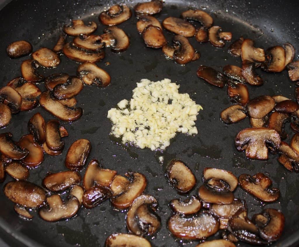 cooked mushrooms in skillet with minced garlic in the middle
