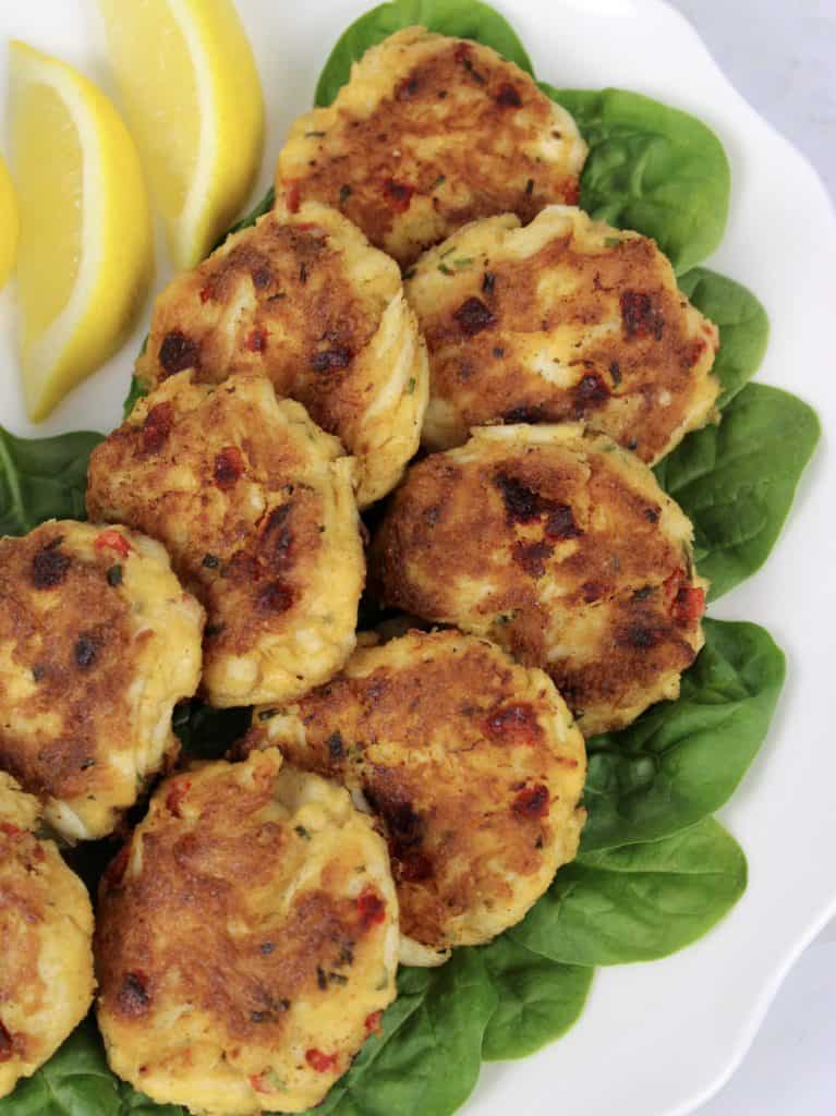 closeup overhead view of crab cakes over bed of spinach with lemon on side