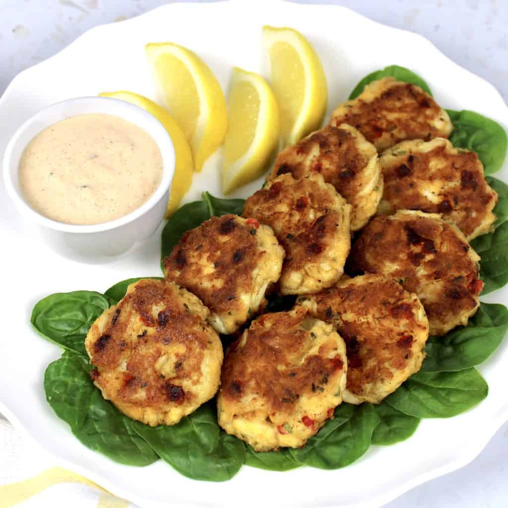 crab cakes on white plate with lemon sides and sauce on side
