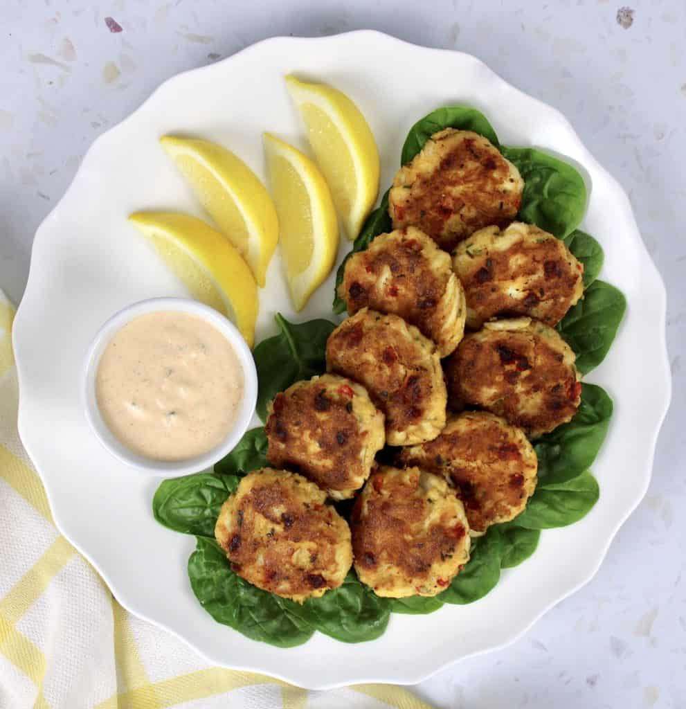crab cakes on white plate with lemon sides and sauce on side