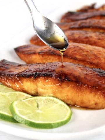 Maple Glazed Salmon on white plate with maple syrup being spooned over top