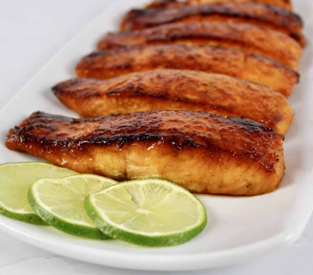 pieces of maple glazed salmon on white plate with lime slices