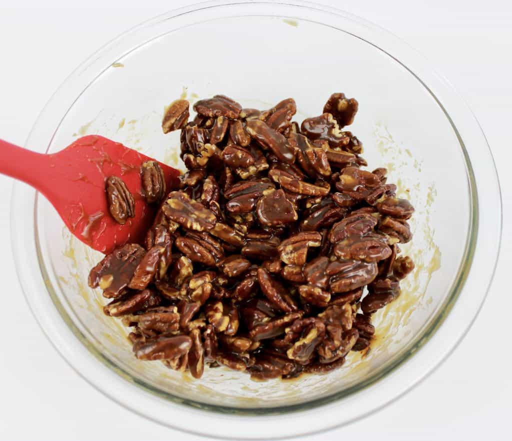 caramel coated pecan in glass bowl with red spatula