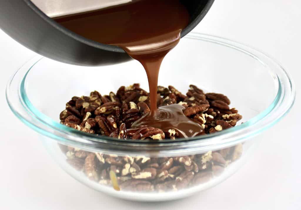 caramel sauce being pour over pecans in glass bowl