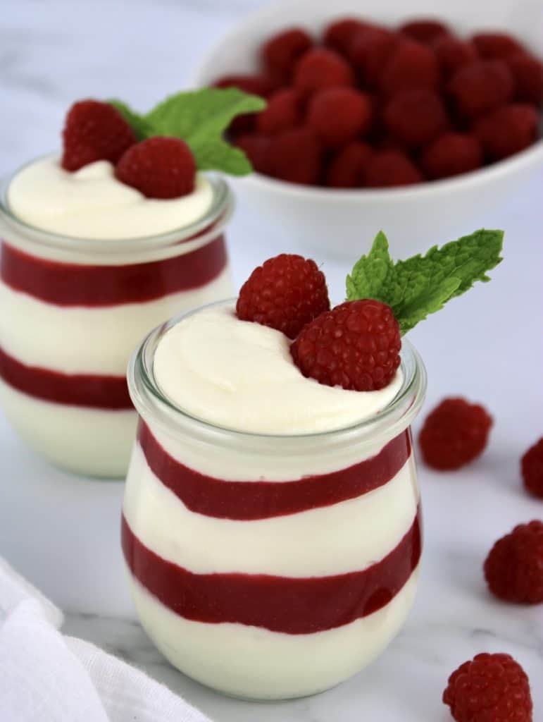 Keto Raspberry White Chocolate Mousse layered in two glass jars with raspberries in background