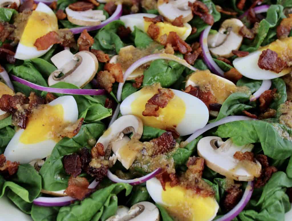 closeup of spinach salad with hot bacon dressing on top