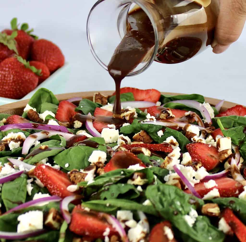 Strawberry Spinach Salad with Balsamic Vinaigrette in wooden bowl with balsamic dressing being poured on top