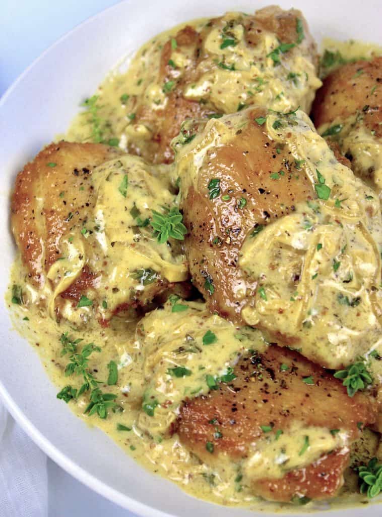 Creamy Dijon Chicken Thighs in white bowl with sauce and fresh thyme on top