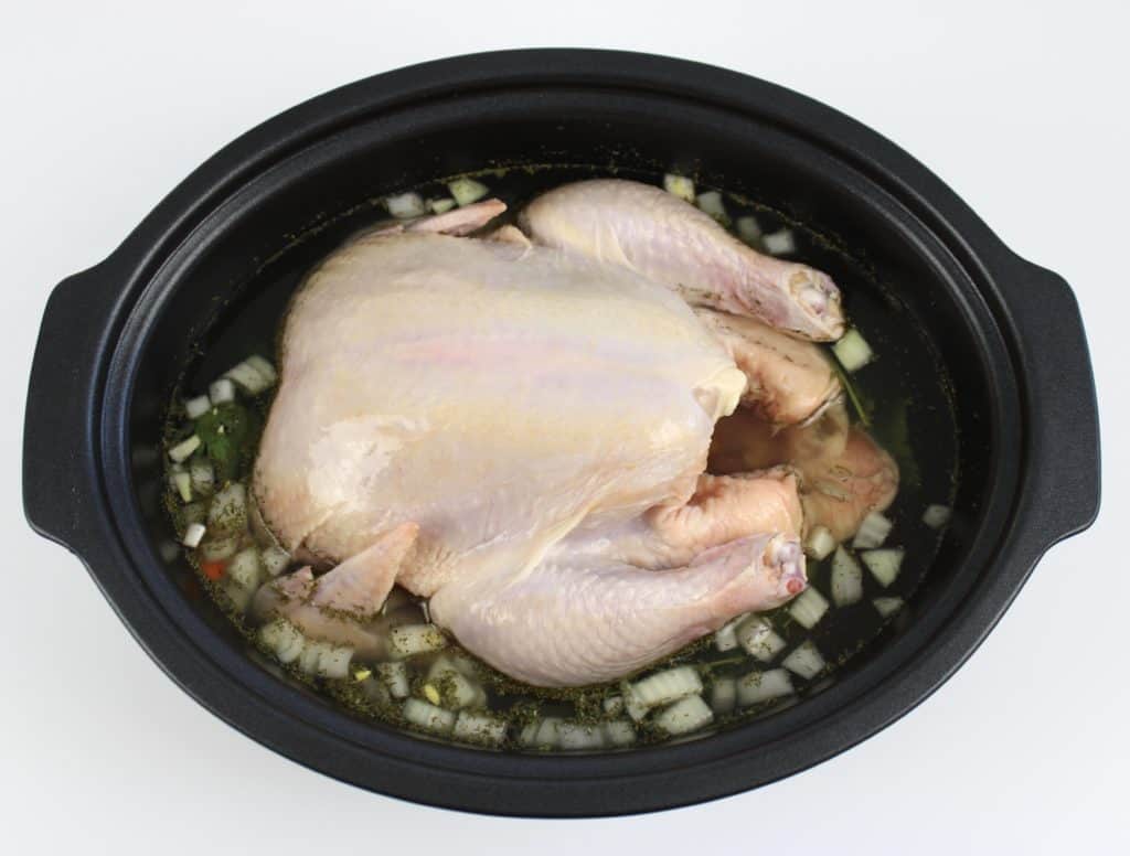 raw whole chicken in crockpot with chopped veggies and broth