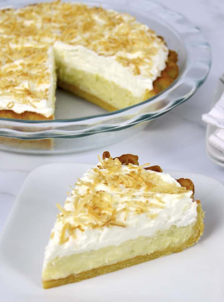 coconut cream pie slice on white plate with pie in background