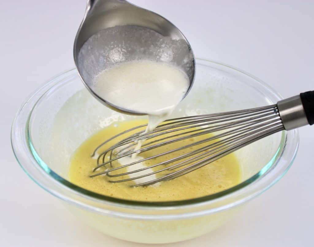 ladle adding heavy cream to bowl with beaten eggs and whisk