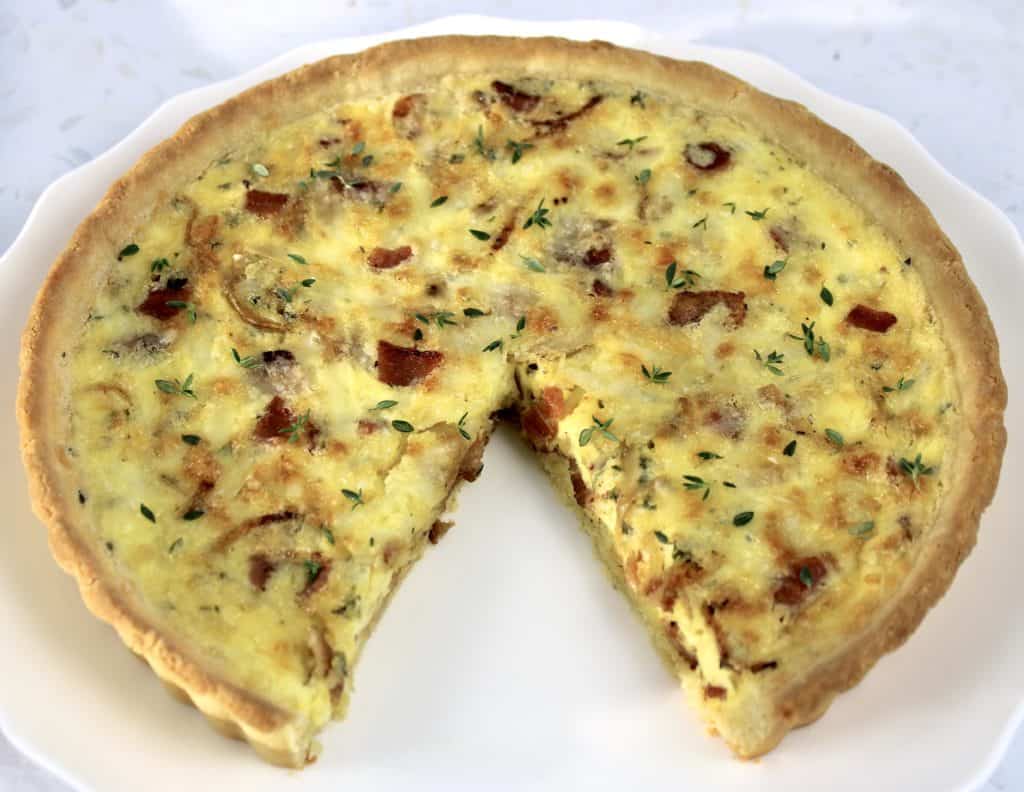 quiche lorraine on white plate with slice missing