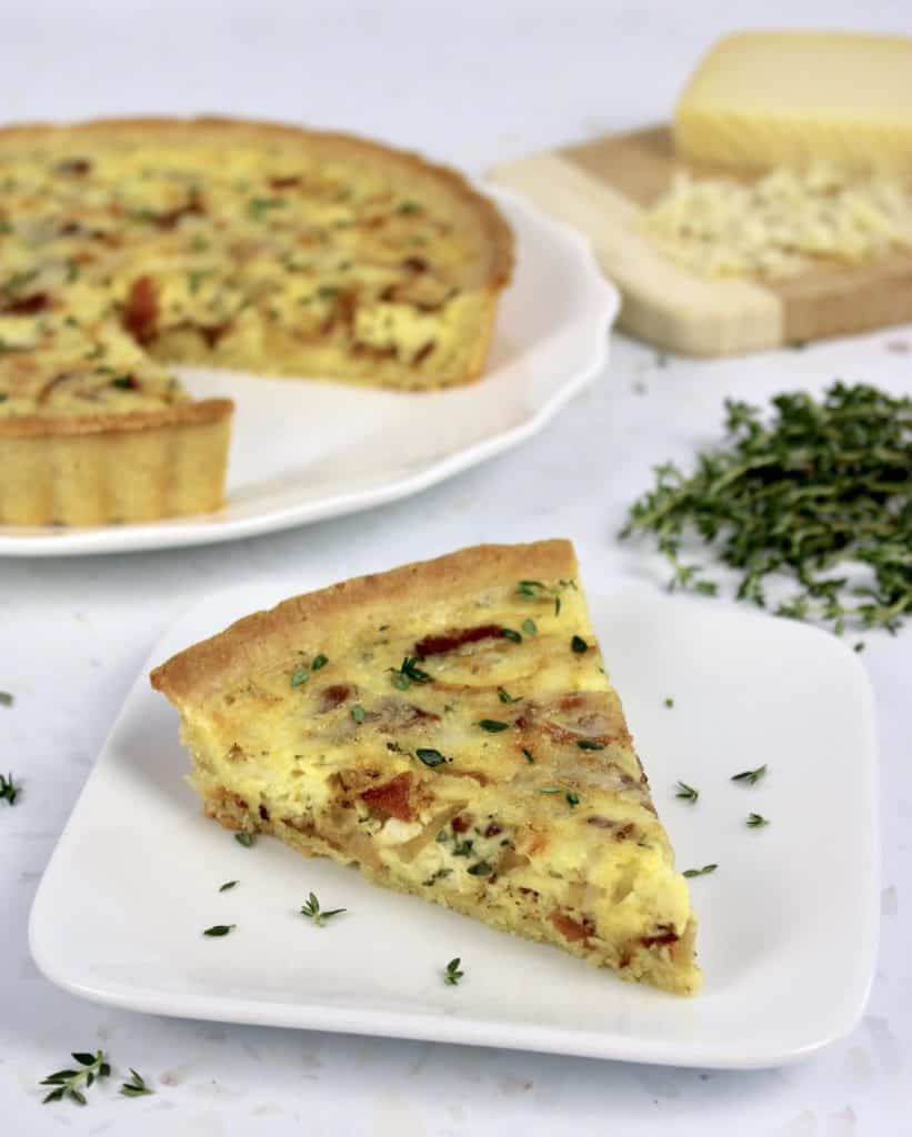 slice of quiche lorraine on white plate with rest of quiche in background