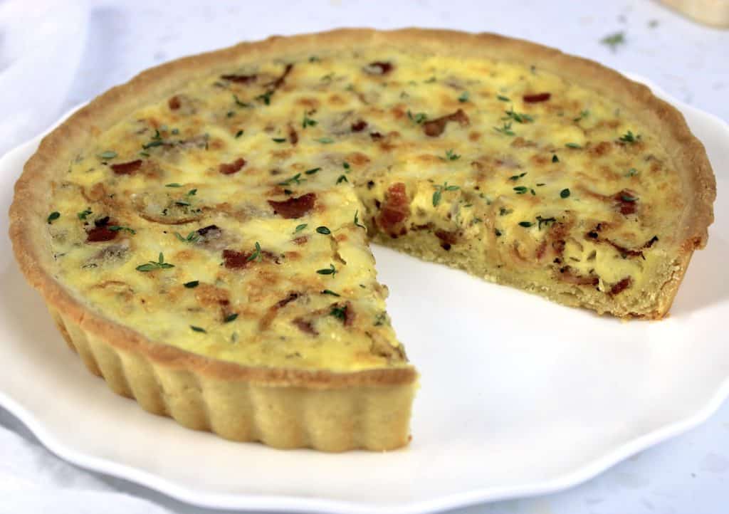quiche lorraine on white plate with slice missing
