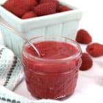 raspberry jam in jar with spoon and raspberries in background