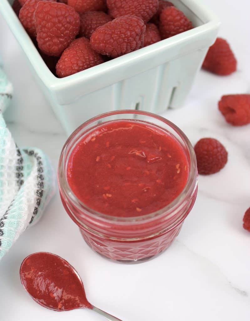 overhead view of raspberry jam in jar with raspberries in background