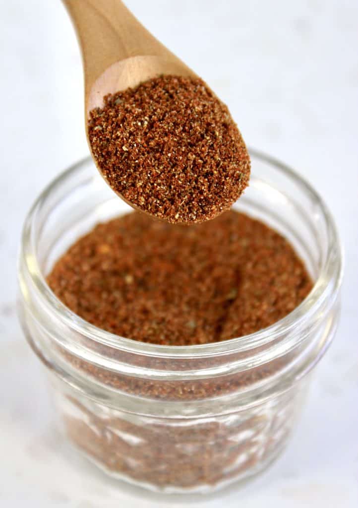 taco seasoning mix in glass jar with wooden spoon holding up some