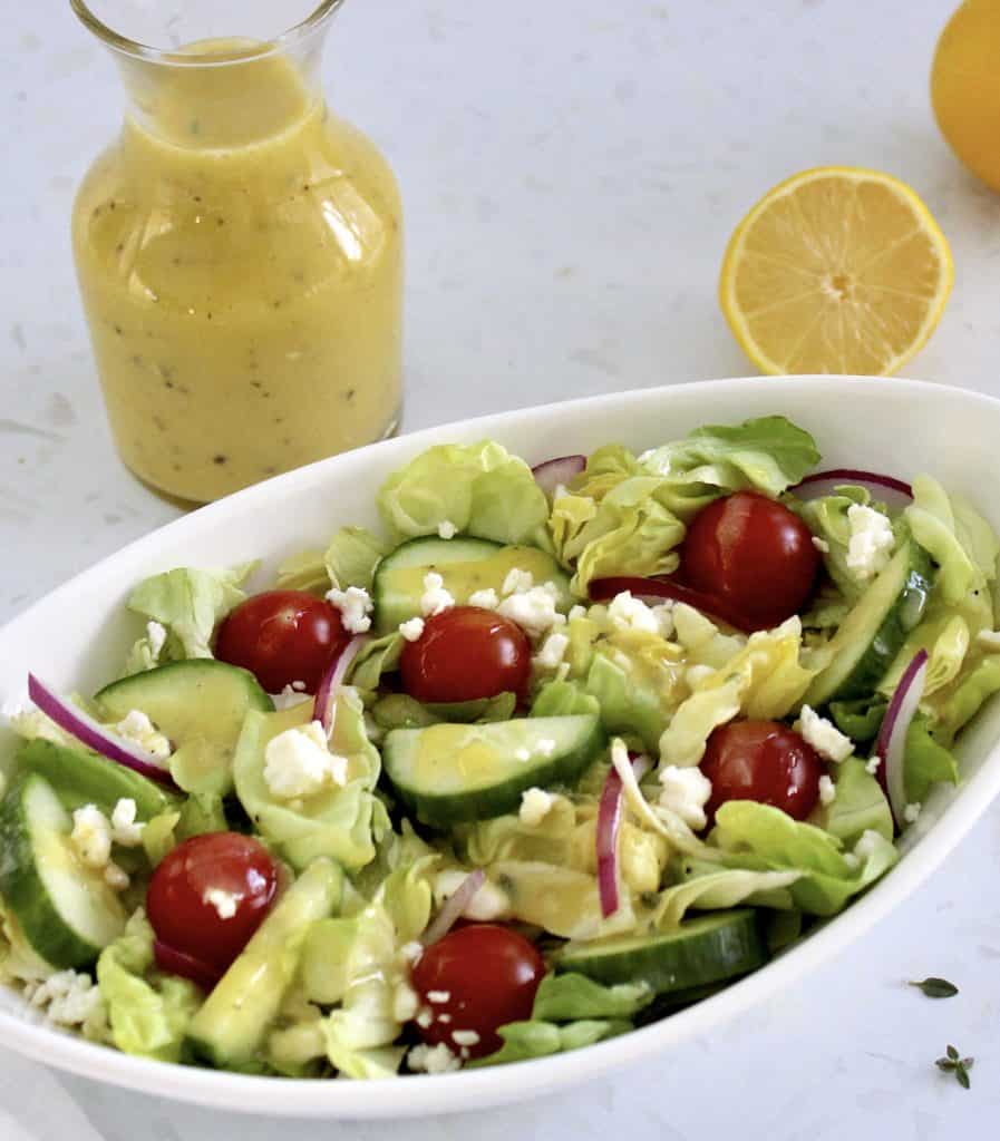 Lemon Vinaigrette over salad in white bowl with dressing in background