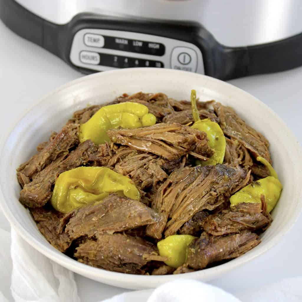 mississippi pot roast with peppers in white bowl crockpot in background