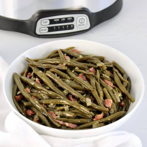 green beans with ham in white bowl crockpot in background