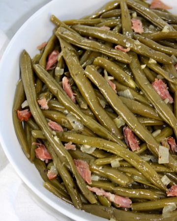 overhead view of cooked green beans with chunks of ham in white bowl