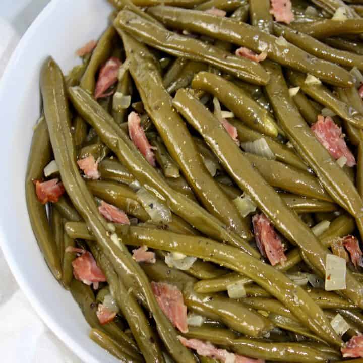 overhead view of cooked green beans with chunks of ham in white bowl