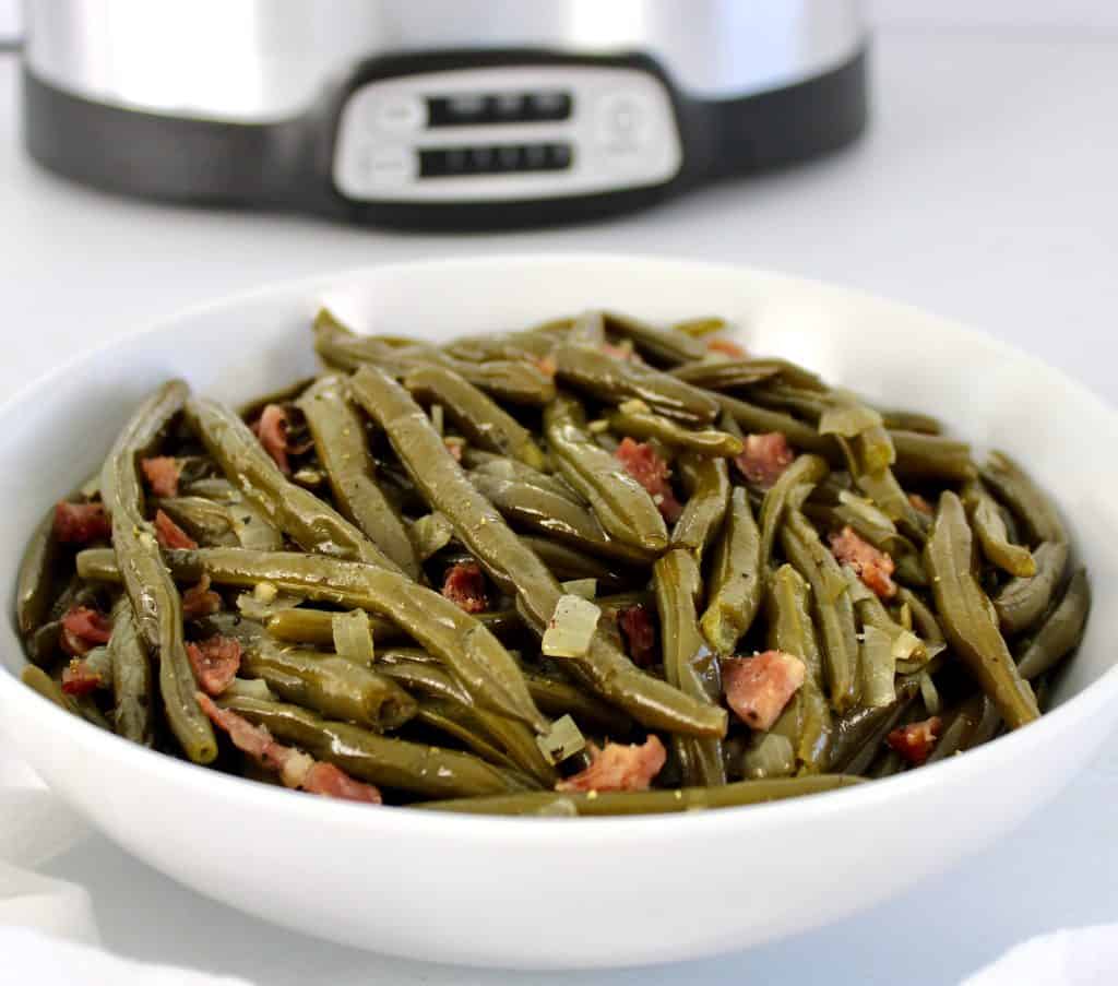 closeup of green beans in white bowl with crockpot in background