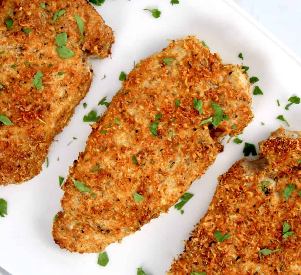 overhead view of breaded pork chops on white plate with parsley