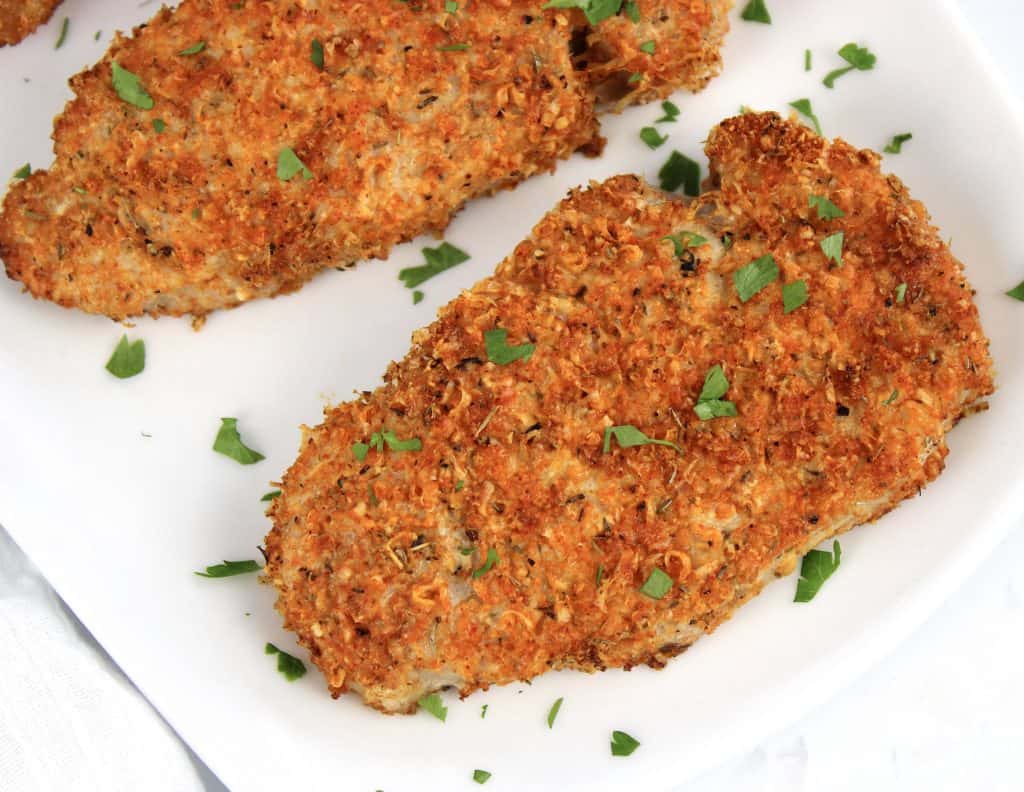 breaded air fryer pork chops on white plate with parsley garnish