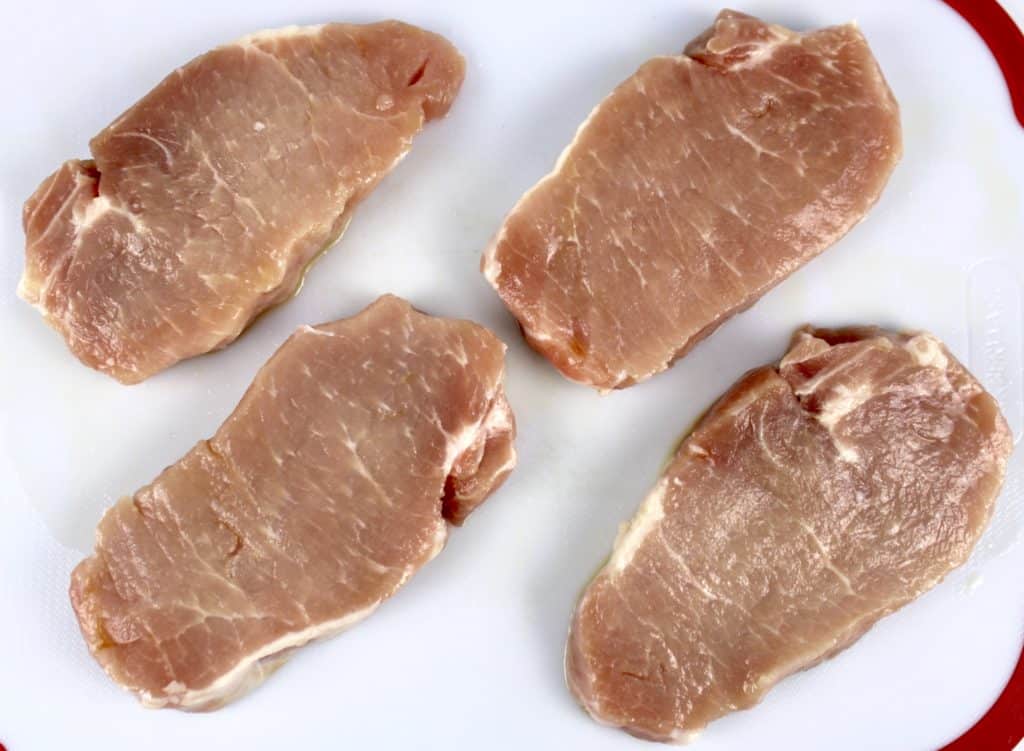 4 pork chops coated in olive oil on white cutting board