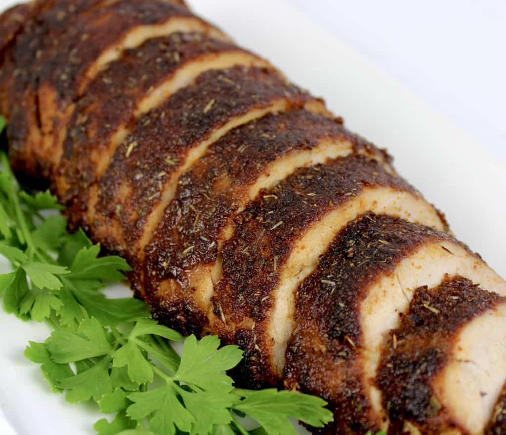 pork tenderloin with seasoned crust sliced on white plate with parsley on side