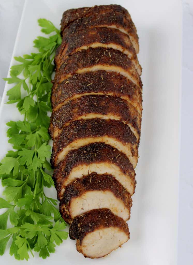 overhead view of sliced pork tenderloin on white plate with parsley garnish