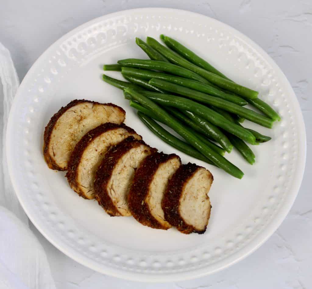 overhead view of sliced pork tenderloin with green beans on white plate