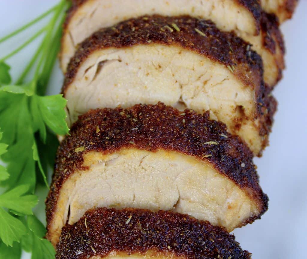 slices of cooked pork tenderloin on white plate with parsley garnish