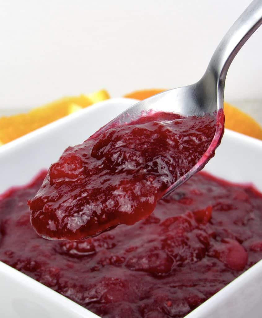 closeup of cranberry sauce in white bowl with spoonful