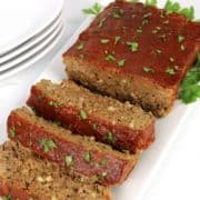 meatloaf partially sliced on white plate with chopped parsley on top