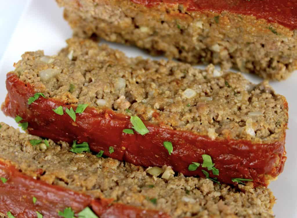 closeup of sliced meatloaf on white plate with parsley garnish