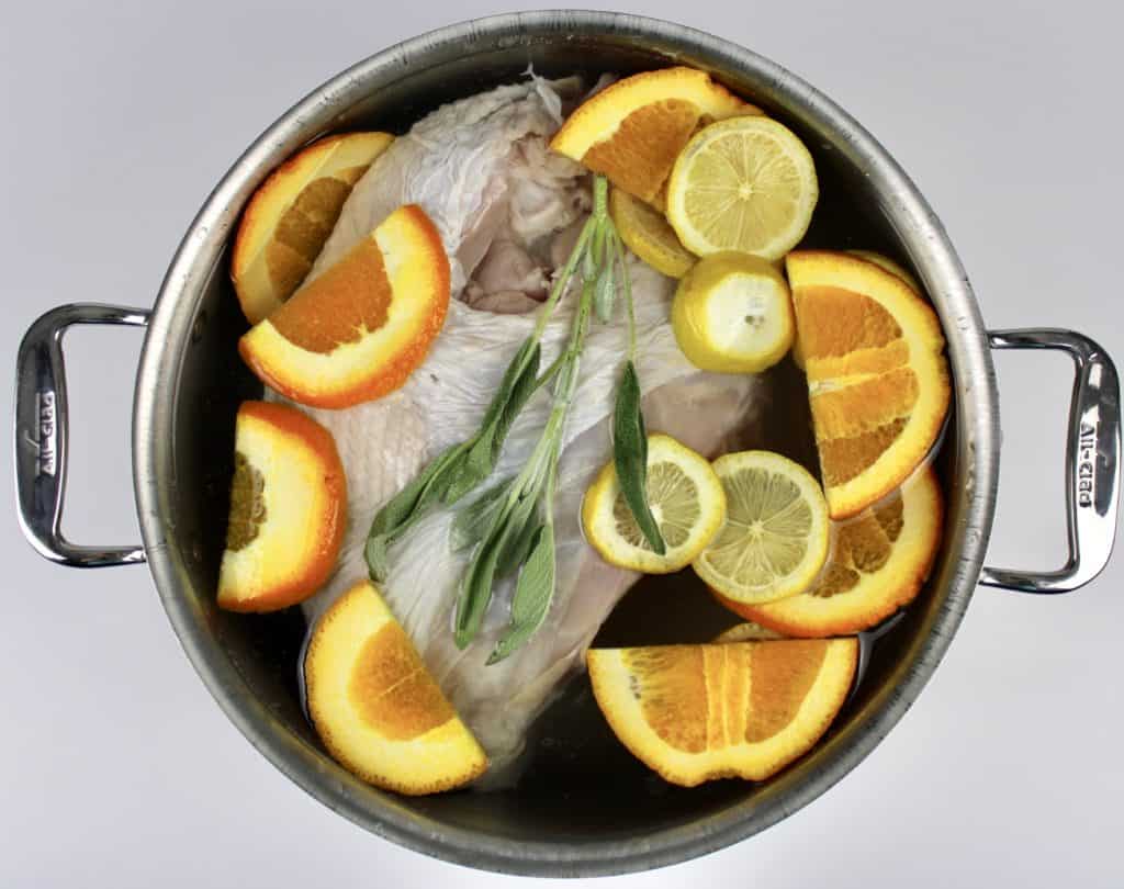 raw turkey in pot with water lemon orange and sage