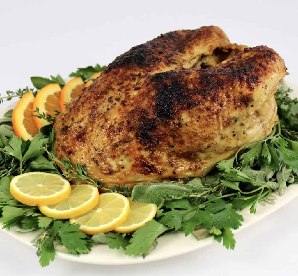 turkey breast on platter with herbs lemon and orange slices around