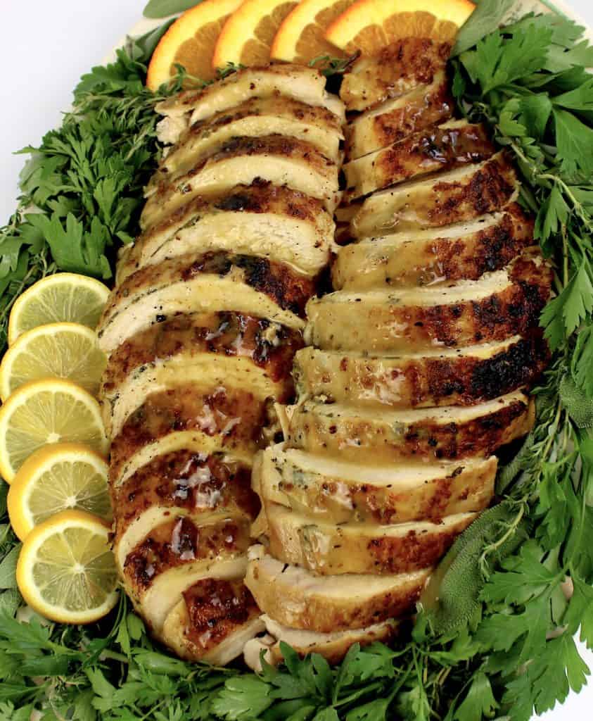sliced turkey breast on platter with gravy on top and herbs around