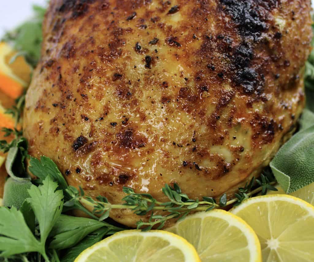 closeup of roasted turkey breast on platter with herbs and lemon slices