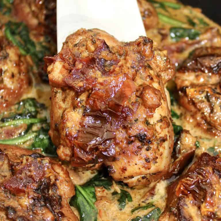 tuscan chicken held up with spatula over cream sauce