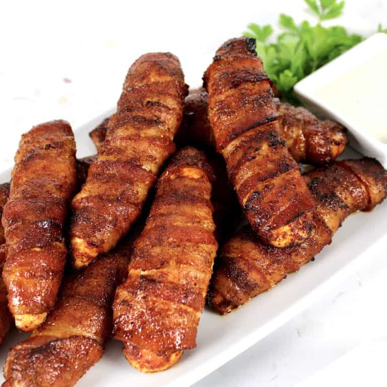 Bacon Wrapped Chicken Tenders on white plate with dipping sauce on side