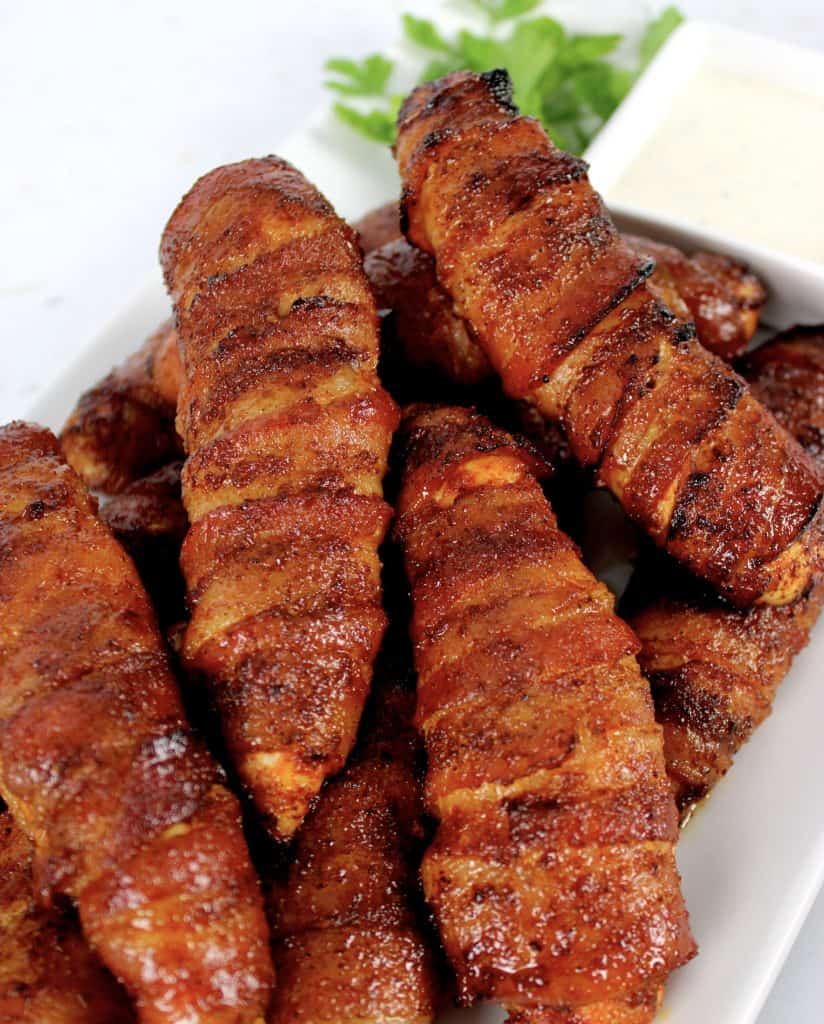 Bacon Wrapped Chicken Tenders on white plate with dipping sauce on side