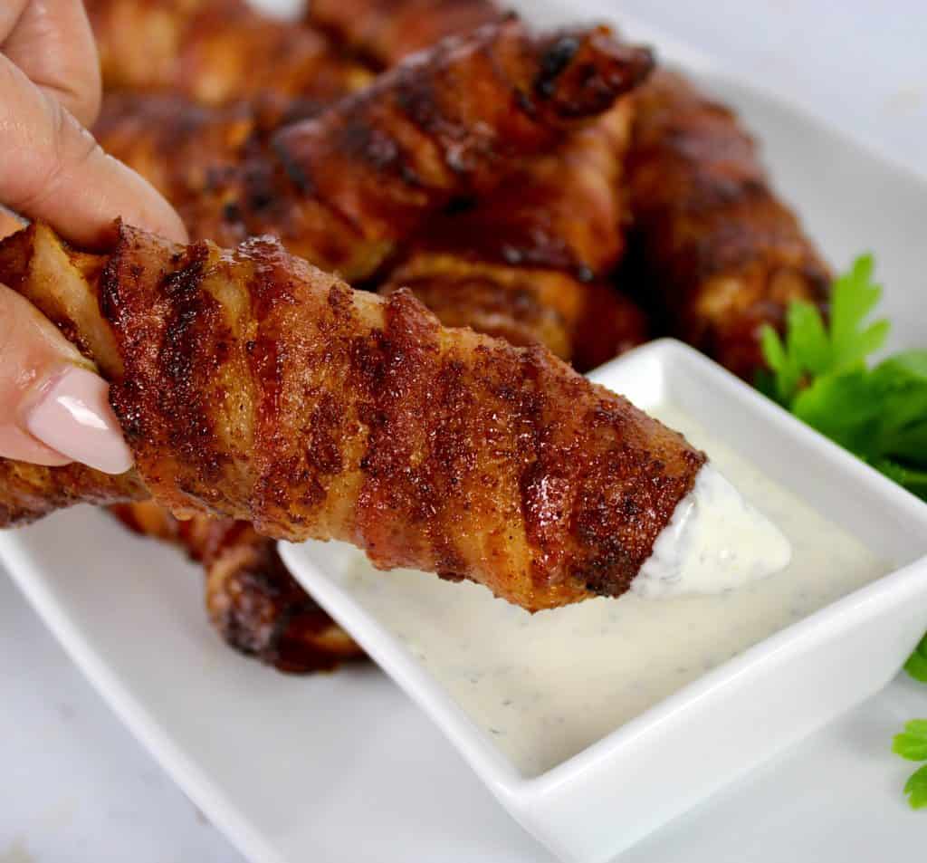 holding up bacon wrapped chicken tender dipped in ranch dressing