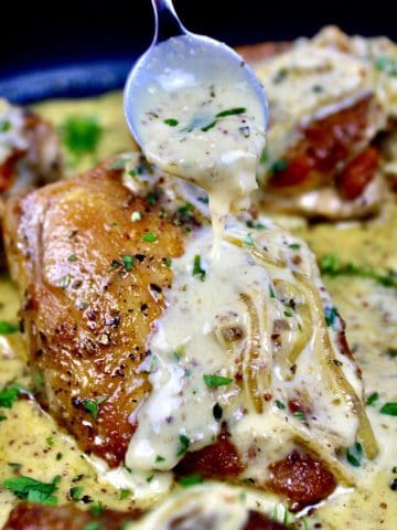 chicken dijon in skillet with sauce being spooned over top