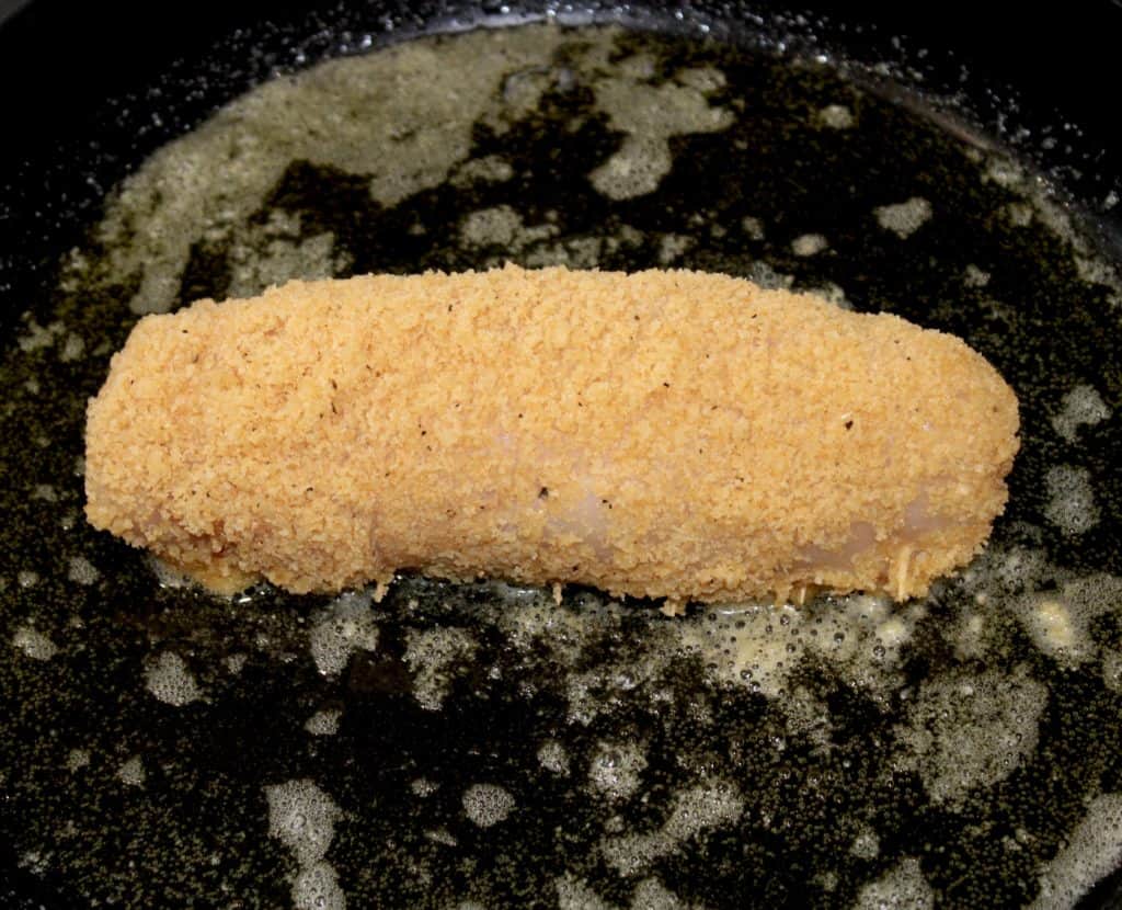 breaded raw chicken breast in skillet cooking